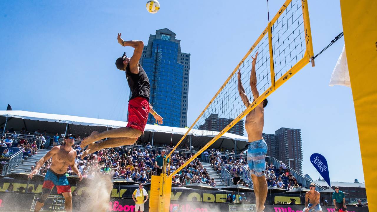 Two beach volleyball teams competing fiercely, with spectators cheering from the sidelines