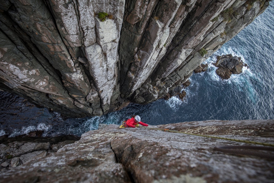 A climber reaches the summit of an icy mountain, camera slung over their shoulder, as they capture the panoramic view of the snow-covered landscape under a crisp blue sky.